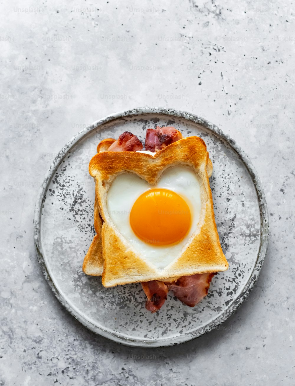 a heart shaped toast with bacon and an egg on top