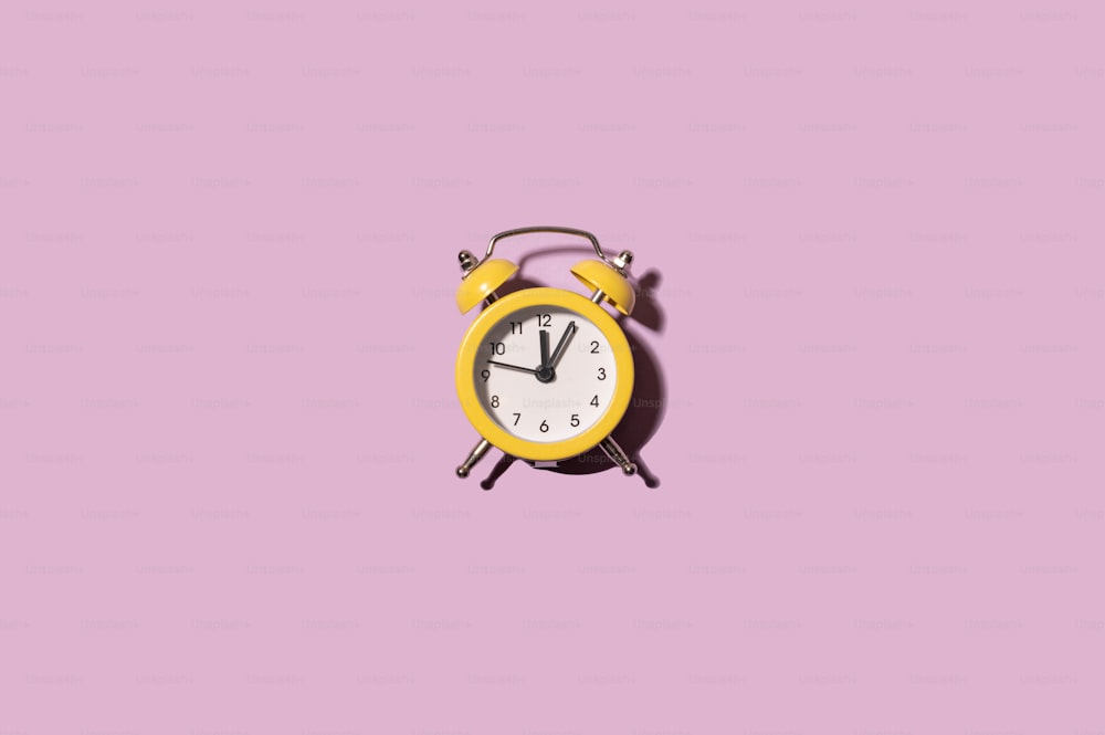 a yellow alarm clock on a pink background