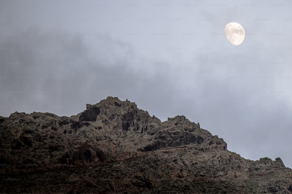 a full moon is seen above a rocky mountain