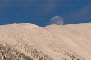 Una luna llena que se eleva sobre una montaña nevada