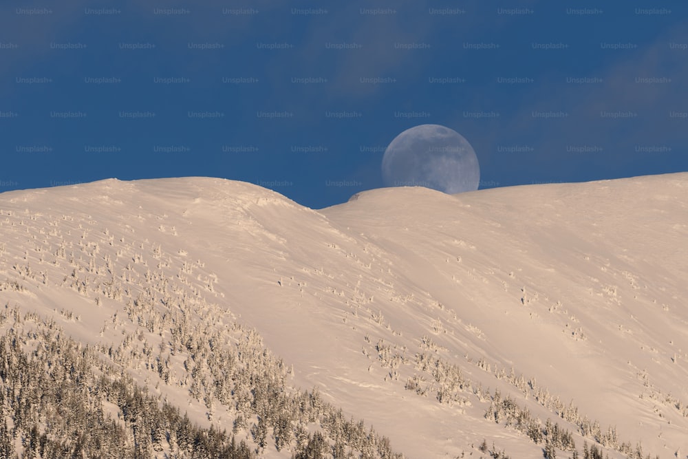 uma lua cheia nascendo sobre uma montanha nevada