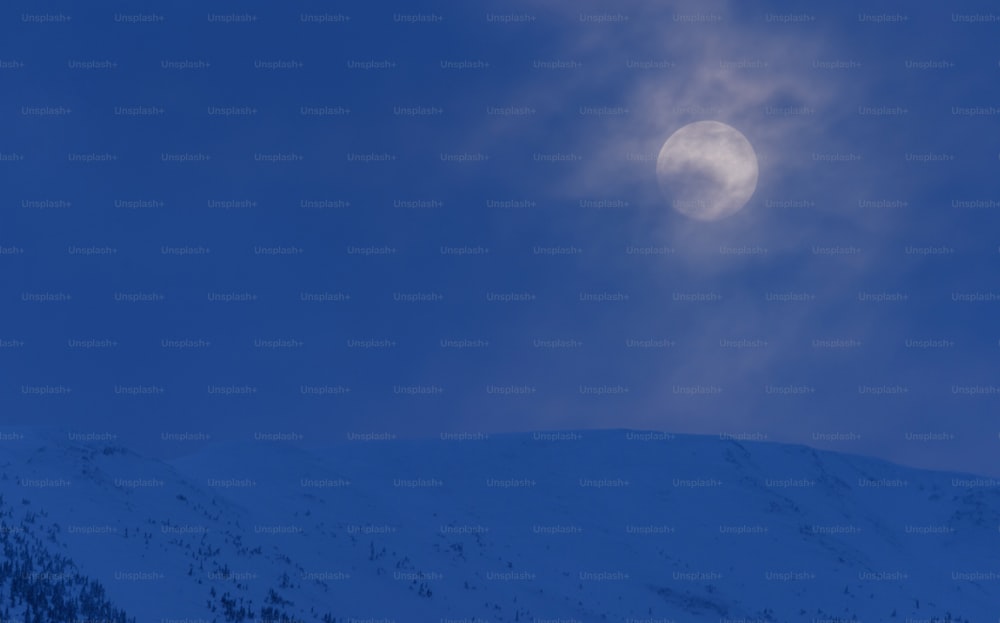 a full moon is seen above a snowy mountain