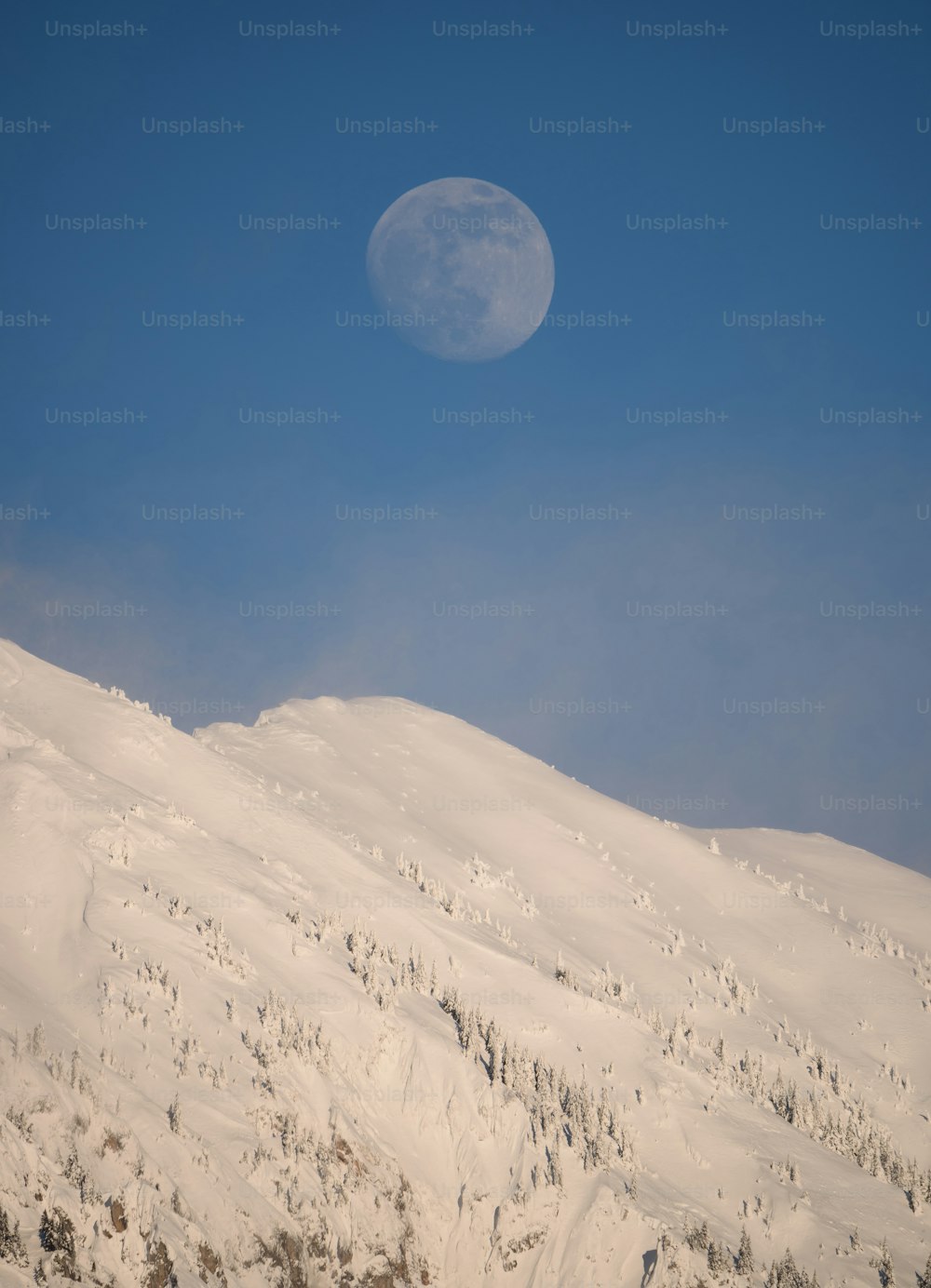 Una luna llena que se eleva sobre una montaña nevada