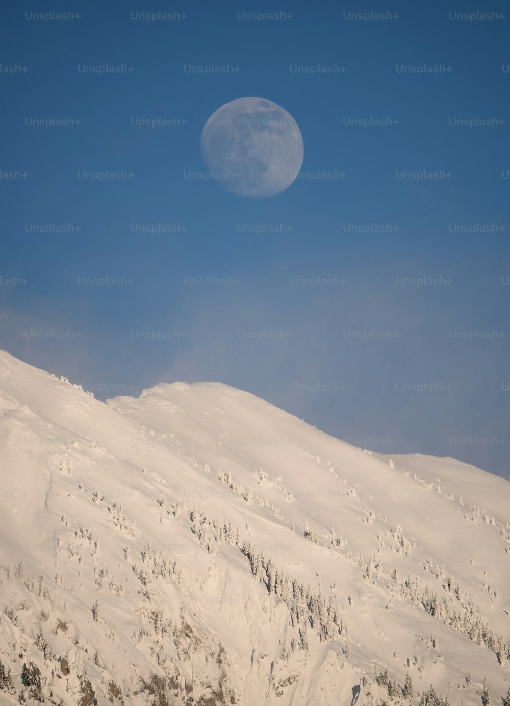 Une pleine lune se levant sur une montagne enneigée