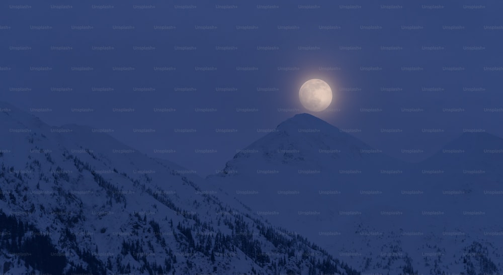 a full moon rising over a snowy mountain range