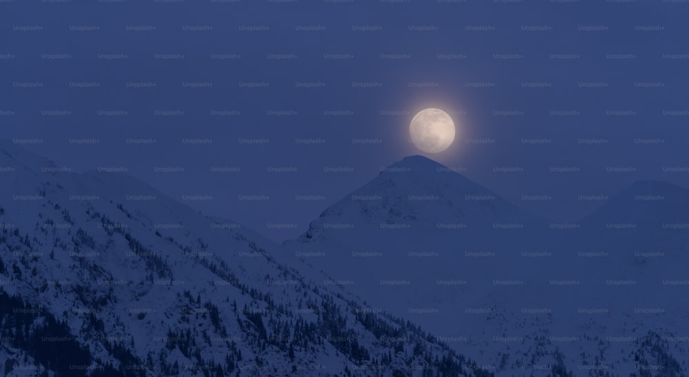 a full moon rising over a snowy mountain range
