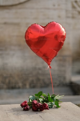 un globo rojo en forma de corazón sentado encima de una losa de cemento