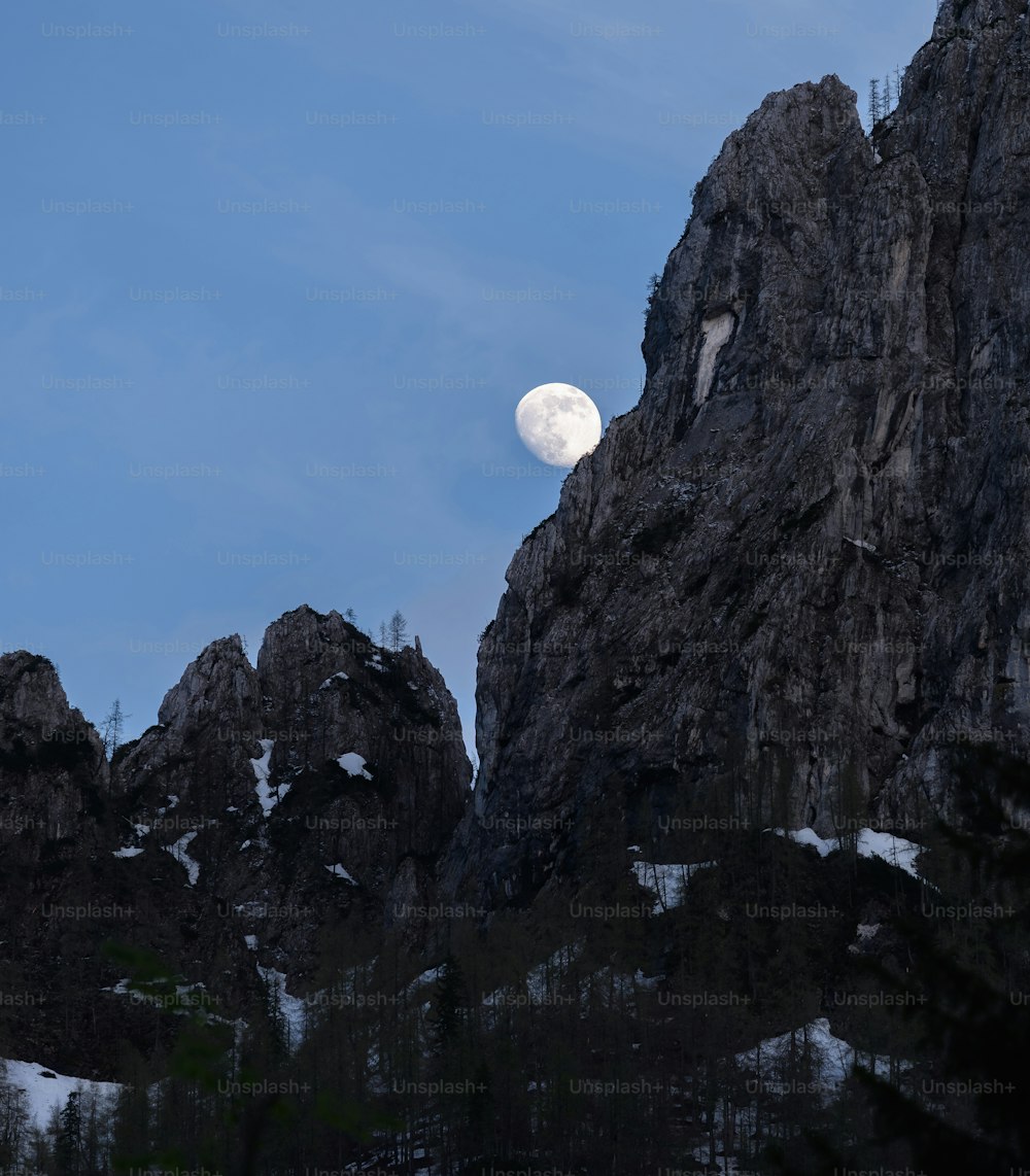 a full moon rises over a rocky mountain