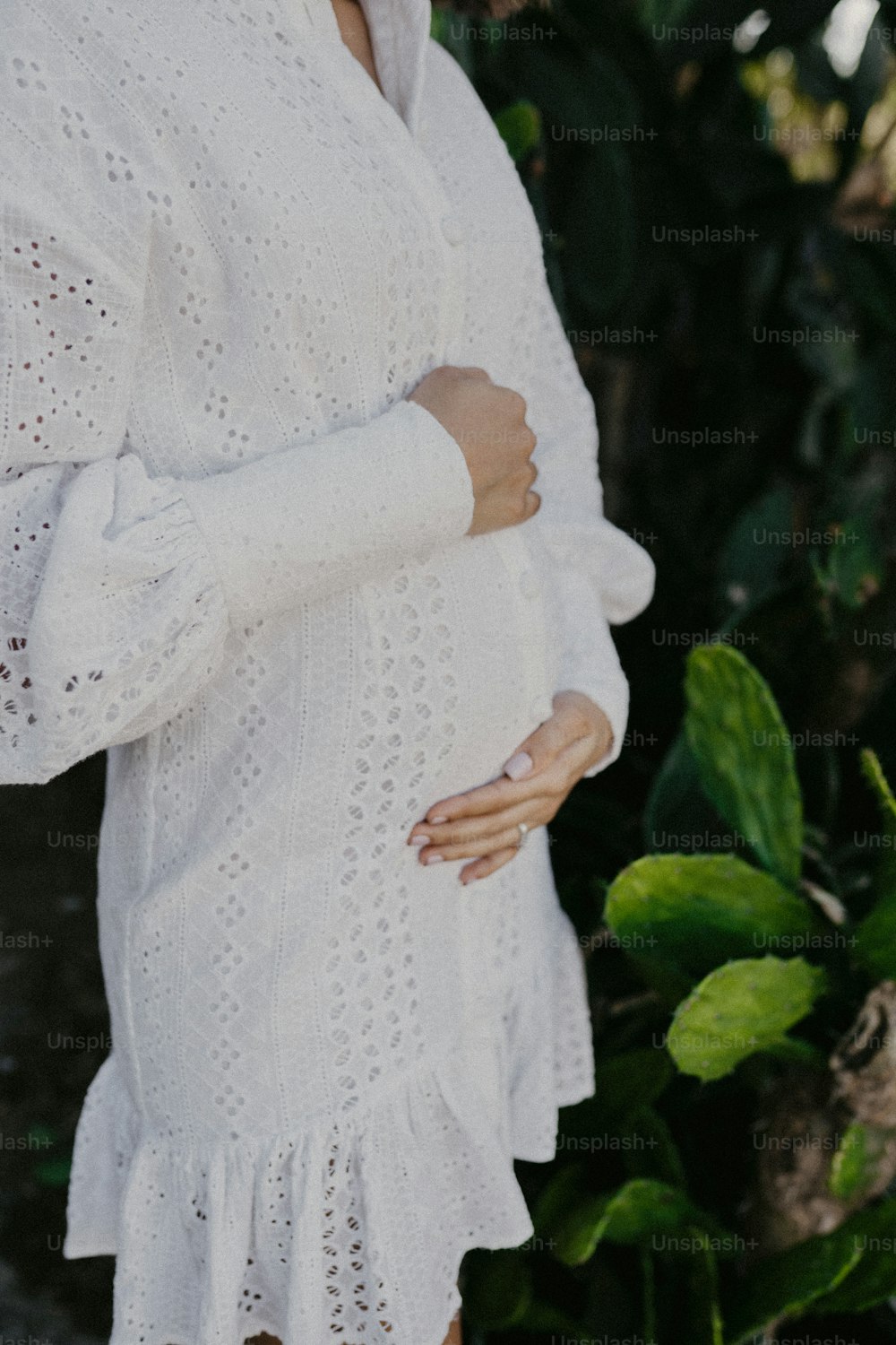 Eine schwangere Frau im weißen Kleid steht vor einem Busch