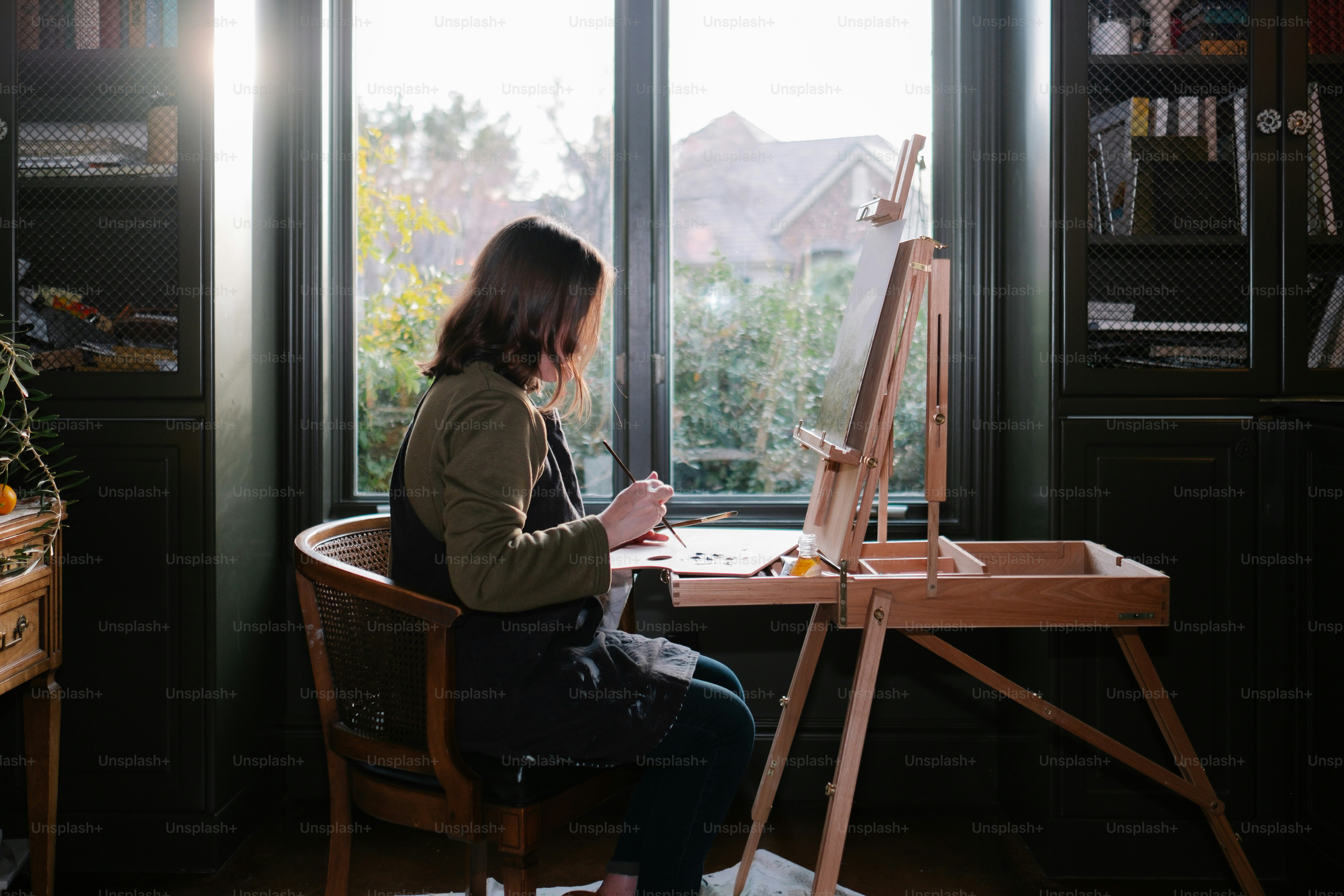 Artist calmly painting or writing near a window with soft morning light, relaxed atmosphere, peaceful creative space