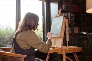 a woman sitting in a chair painting on an easel