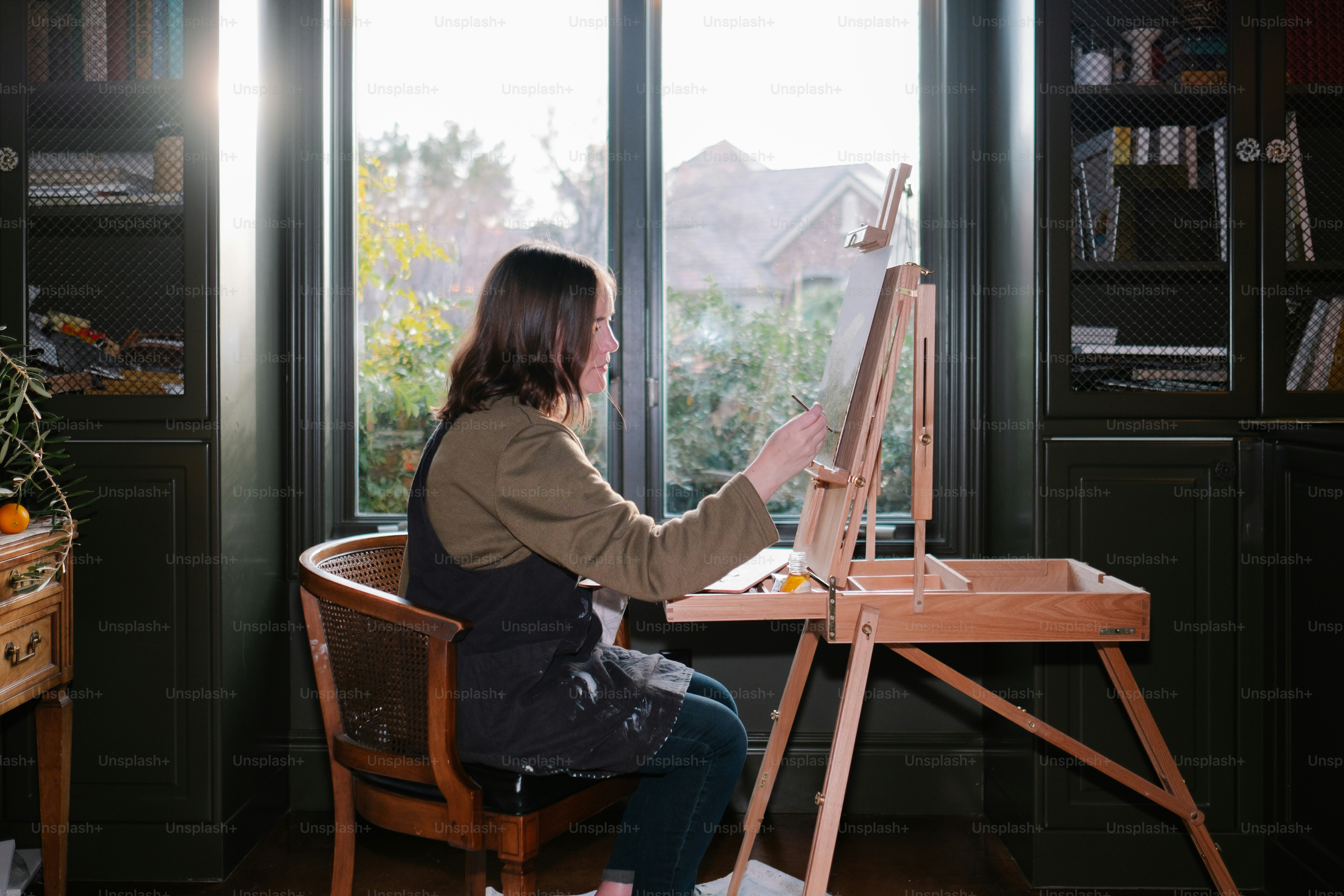 Artist painting or writing near a sunny window, surrounded by calm minimalist workspace, natural light, creative atmosphere