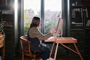a woman sitting in a chair painting on a easel