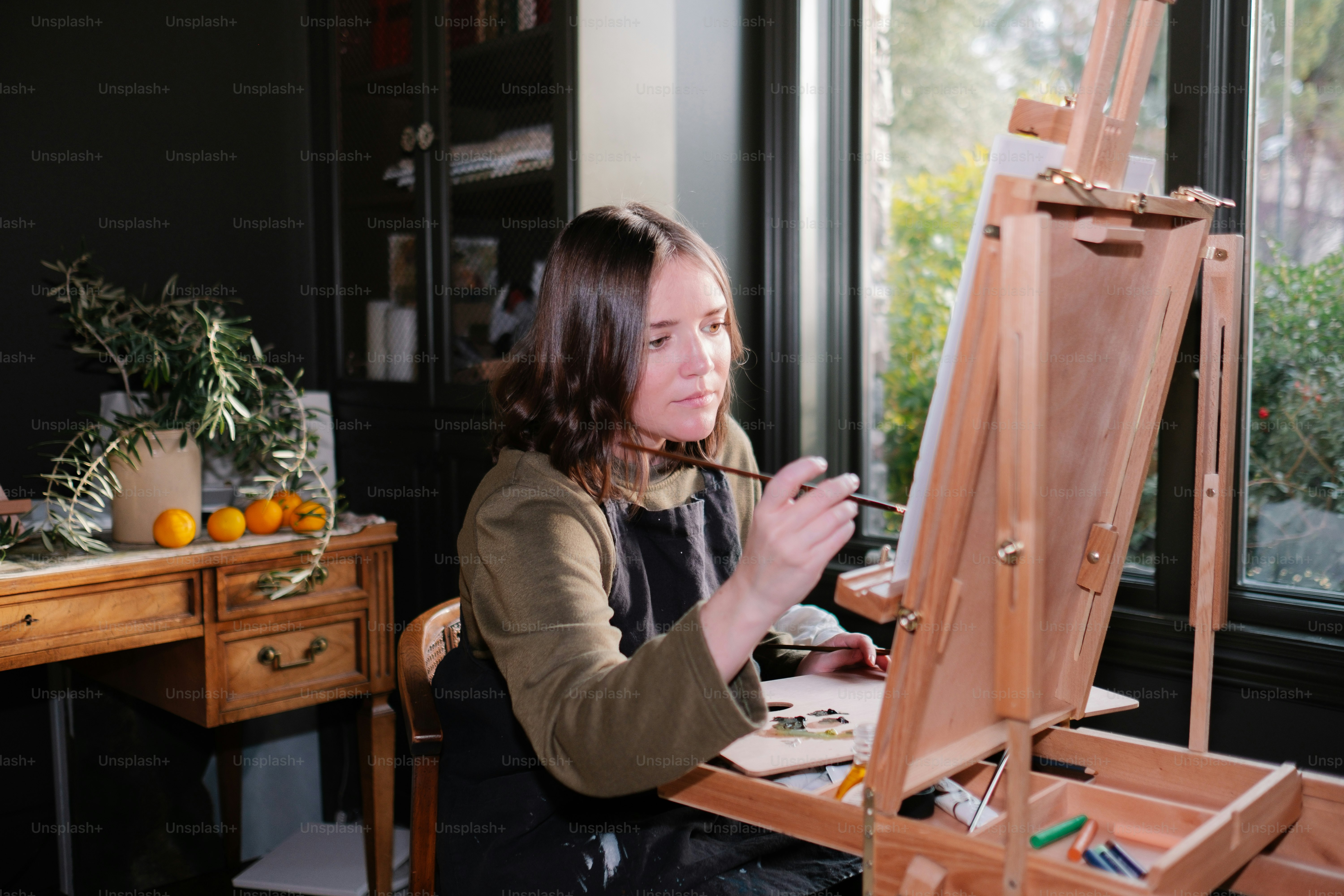 a woman sitting in front of a easel painting