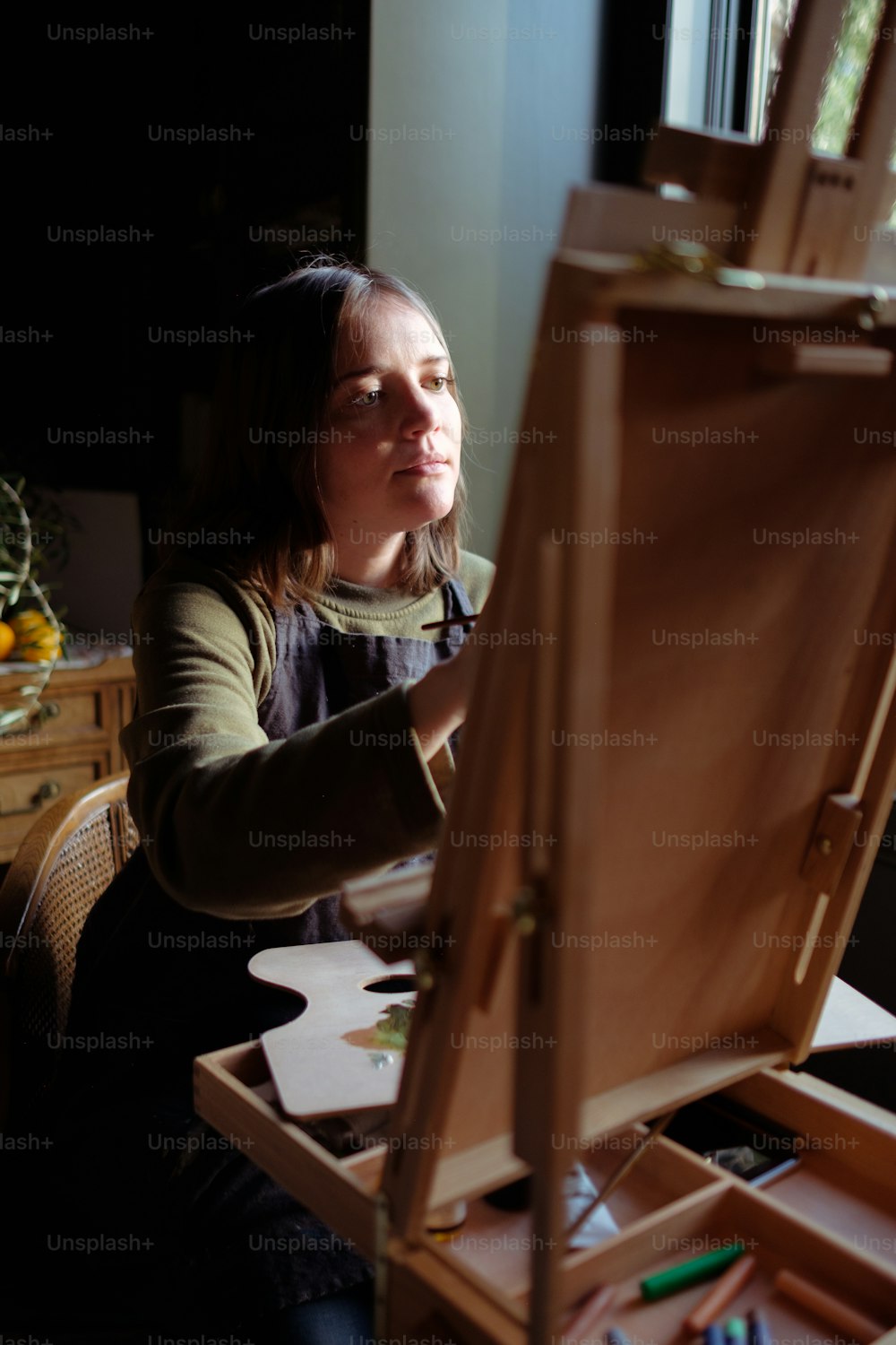 a woman sitting in front of a wooden easel