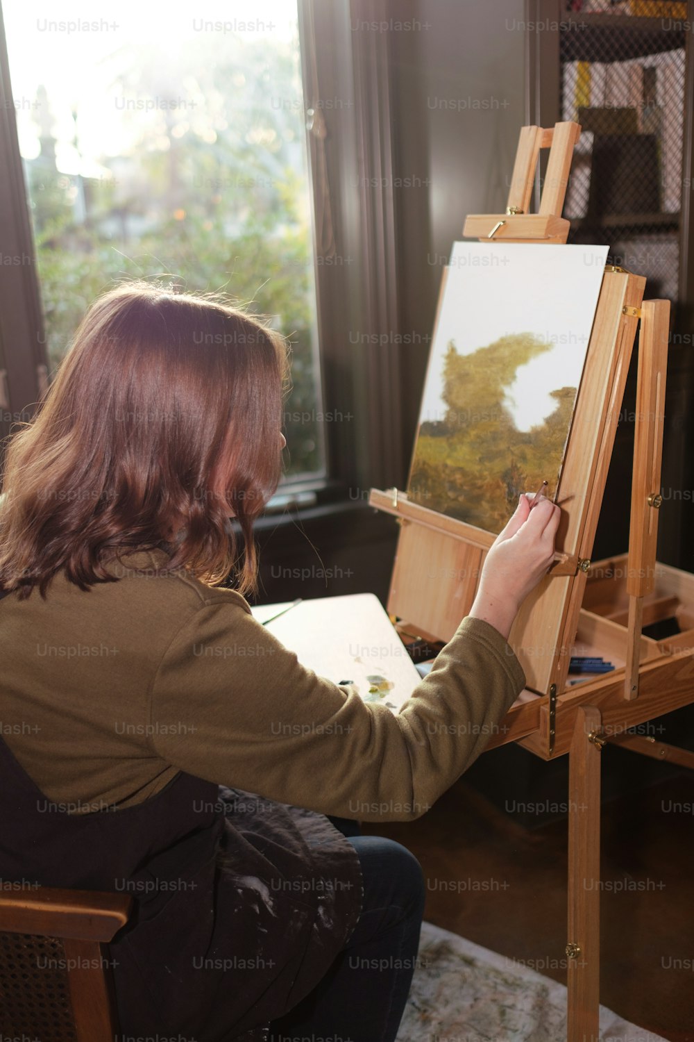 a woman sitting in front of a painting on a easel
