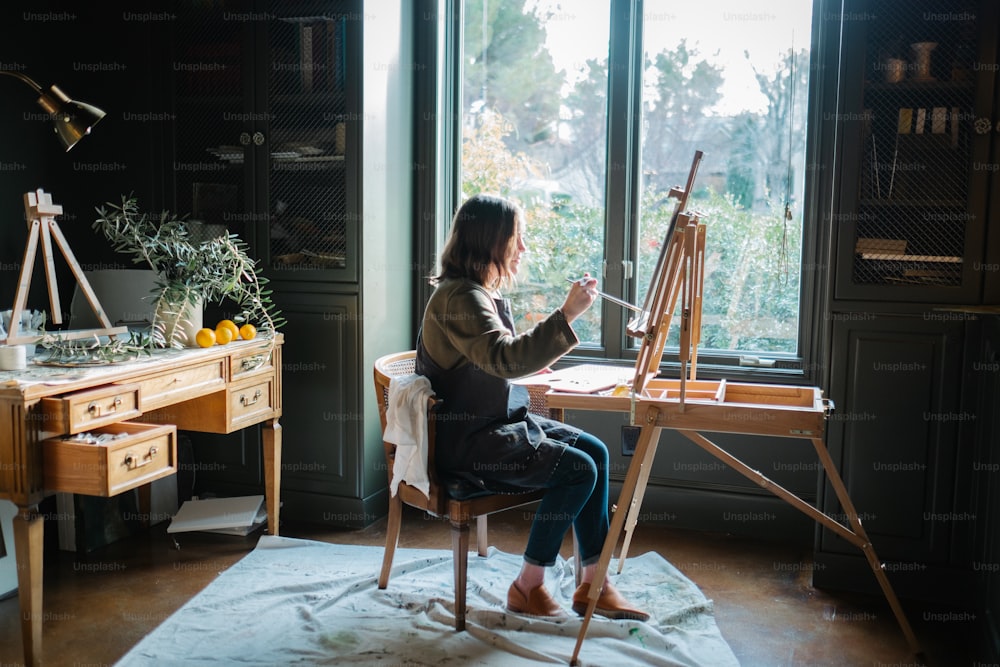 a woman sitting at a desk with an easel in front of a window
