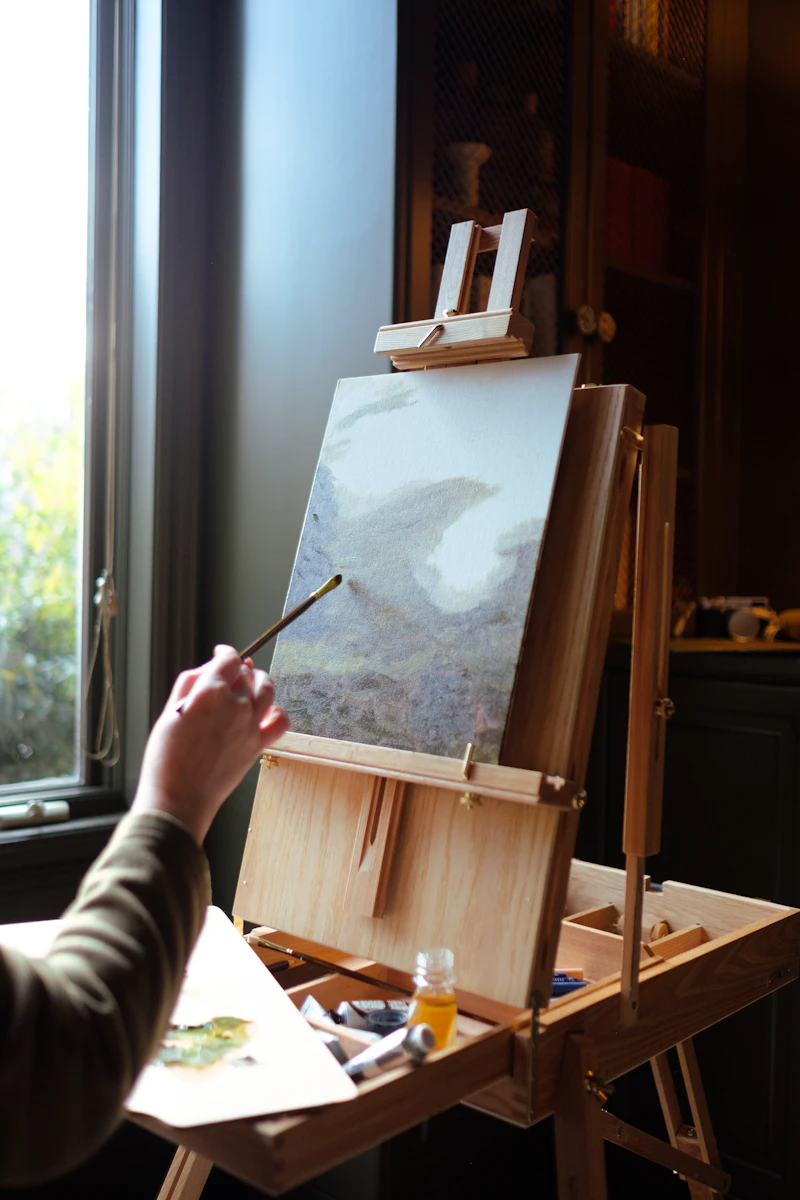 An artist holding a paintbrush before an easel