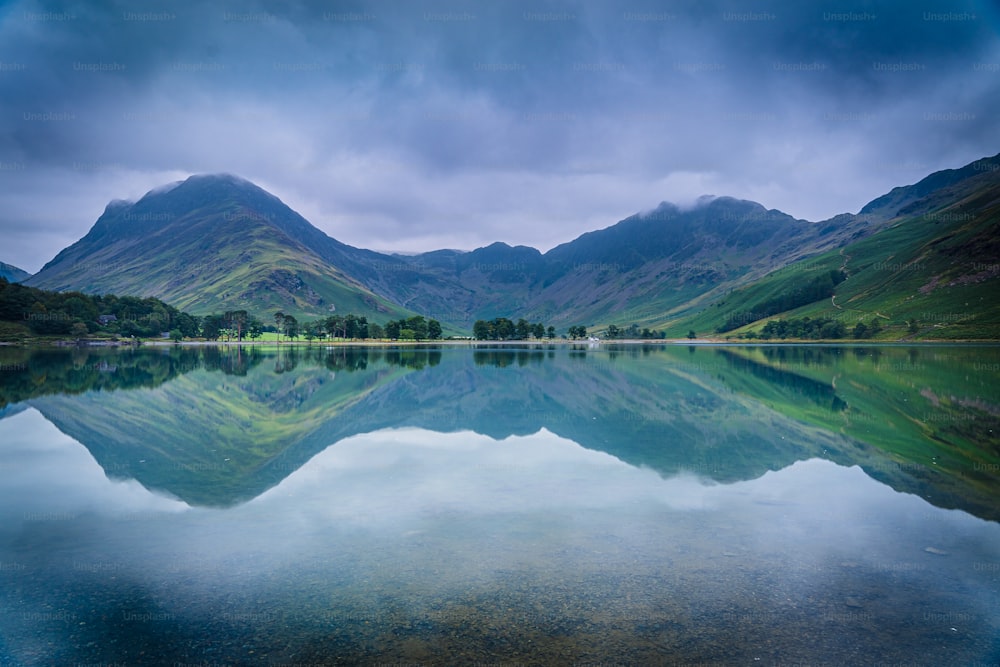 a lake surrounded by mountains under a cloudy sky