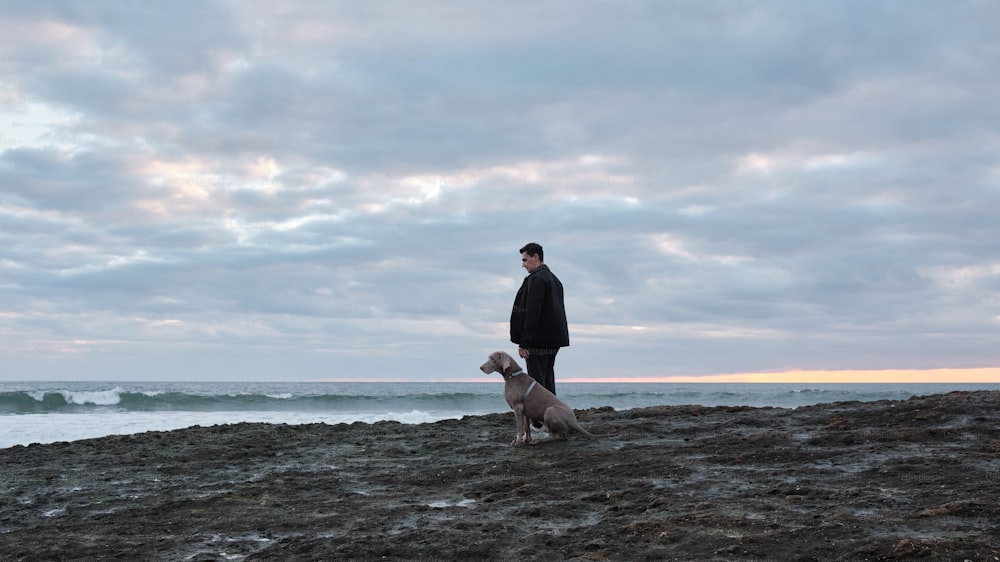 Un hombre parado en la cima de una playa rocosa junto a un perro