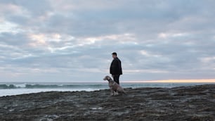 a man standing on top of a rocky beach next to a dog