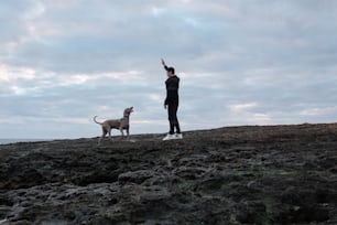 a man standing on top of a rocky beach next to a dog