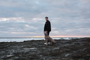 Un hombre parado junto a un perro en una playa rocosa