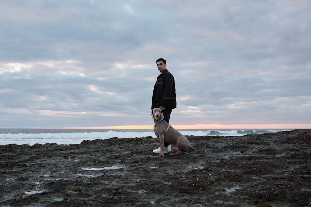 um homem de pé ao lado de um cão em uma praia rochosa