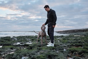 Un homme debout à côté d’un chien sur une plage rocheuse