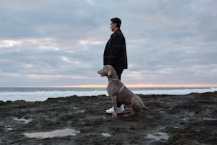 Un uomo in piedi accanto a un cane su una spiaggia rocciosa