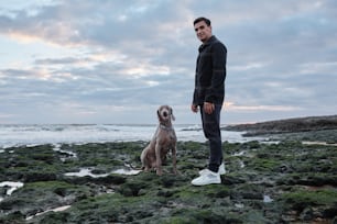 岩だらけのビーチで犬の隣に立っている男