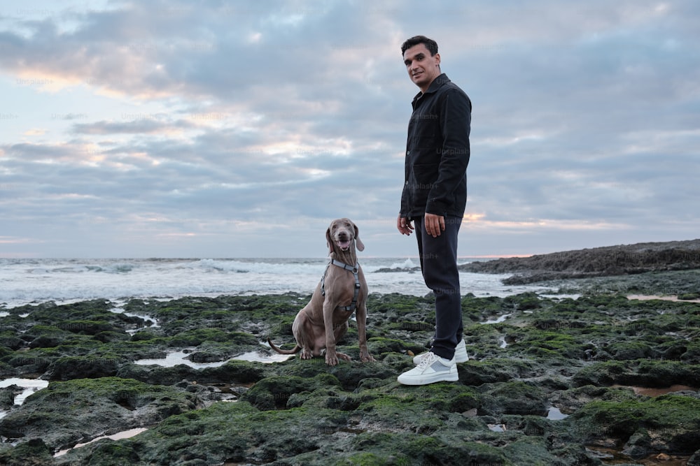 a man standing next to a dog on a rocky beach