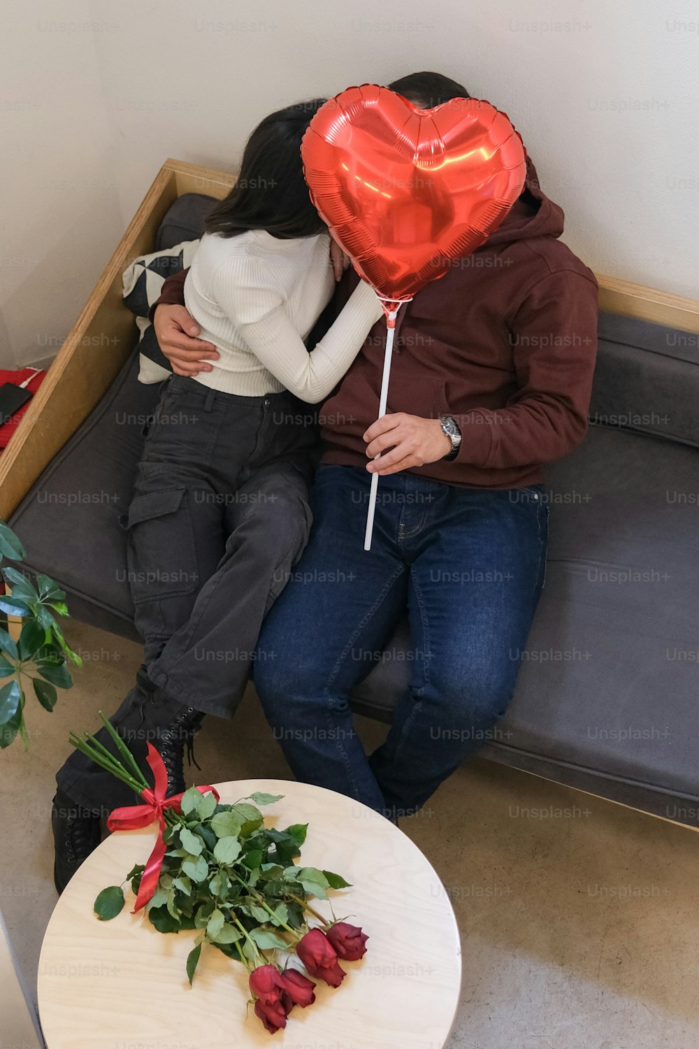 a man and woman sitting on a couch with a heart shaped balloon