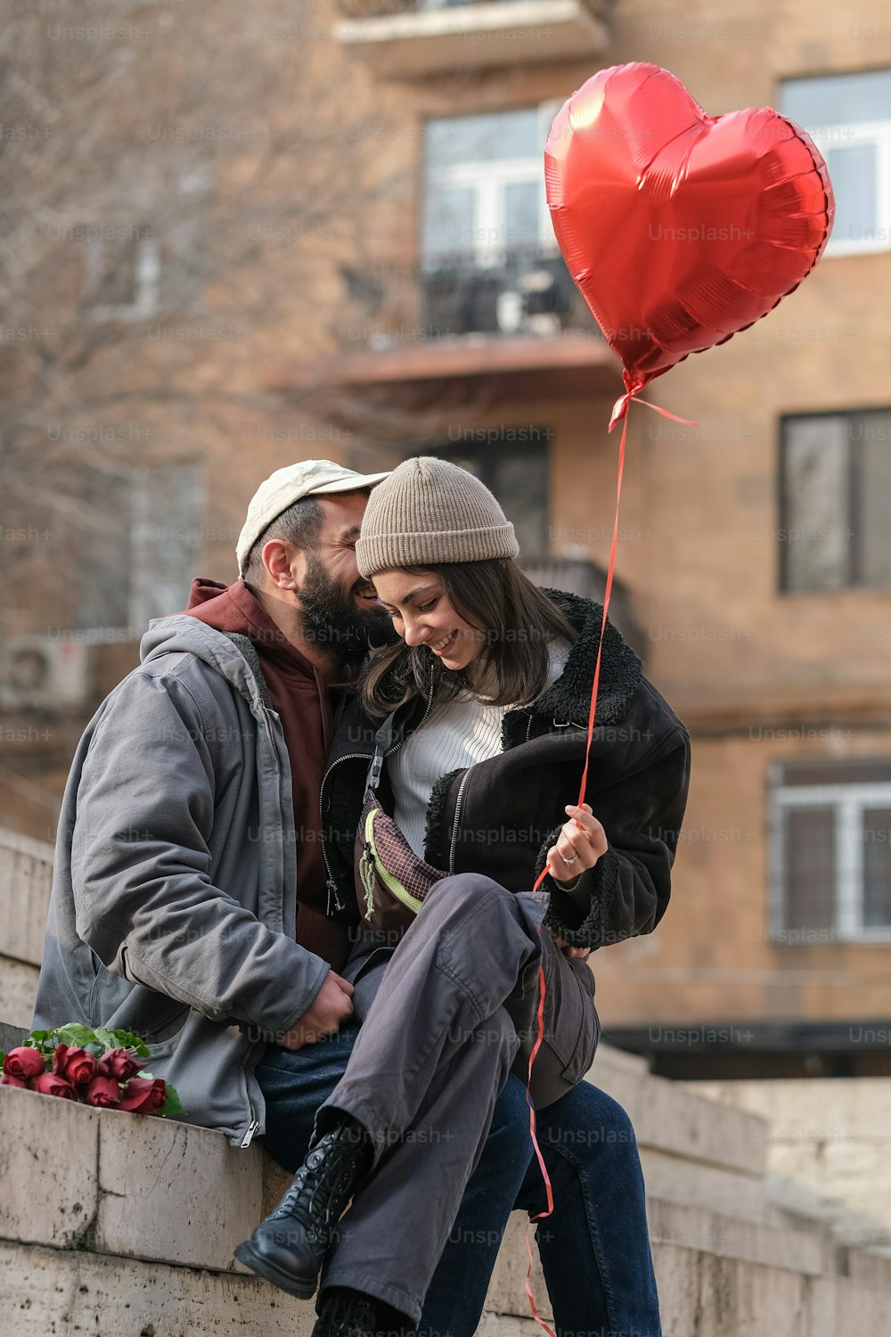 a man and a woman sitting on a wall with a heart shaped balloon