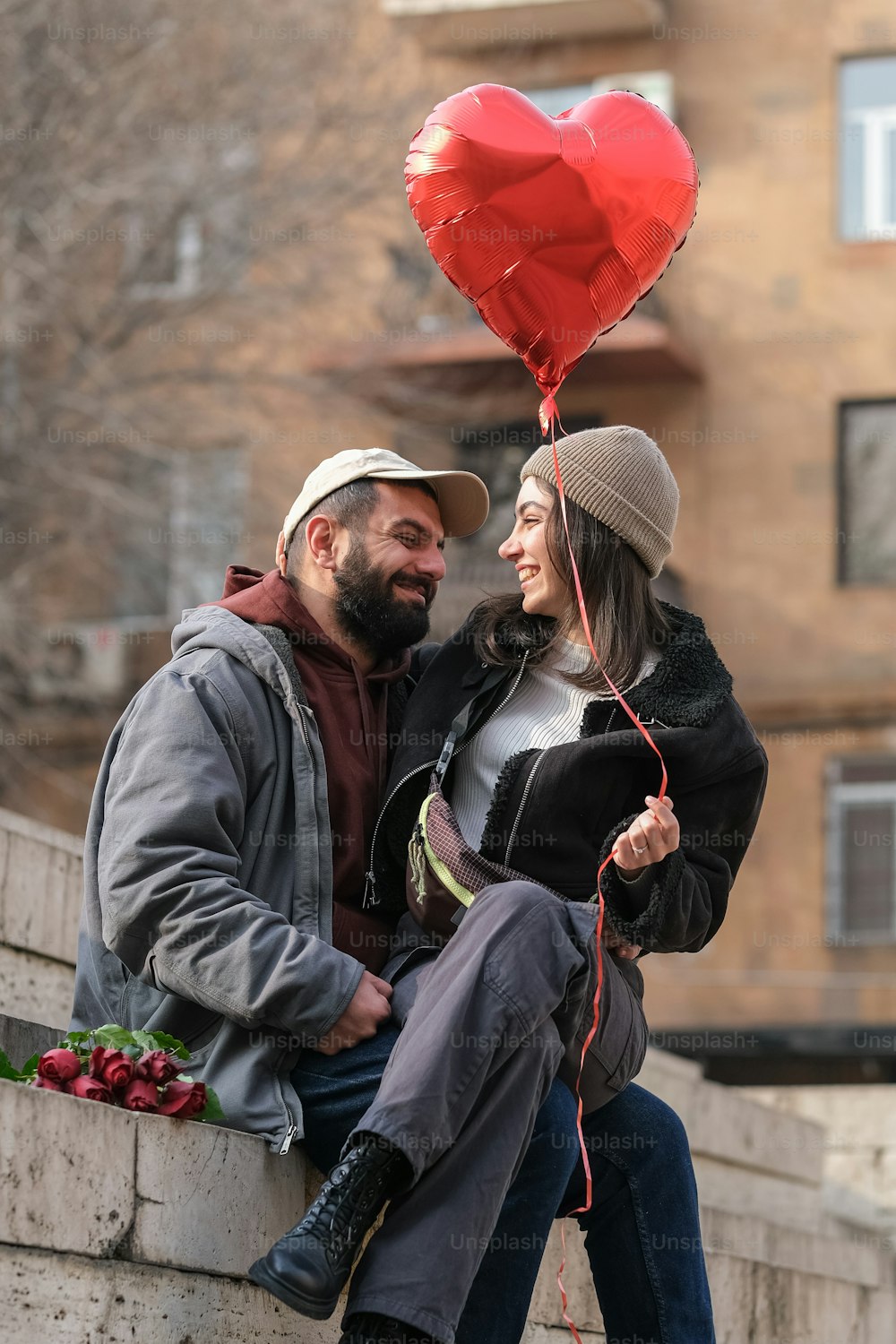 Un hombre y una mujer sentados en una pared con un globo en forma de corazón
