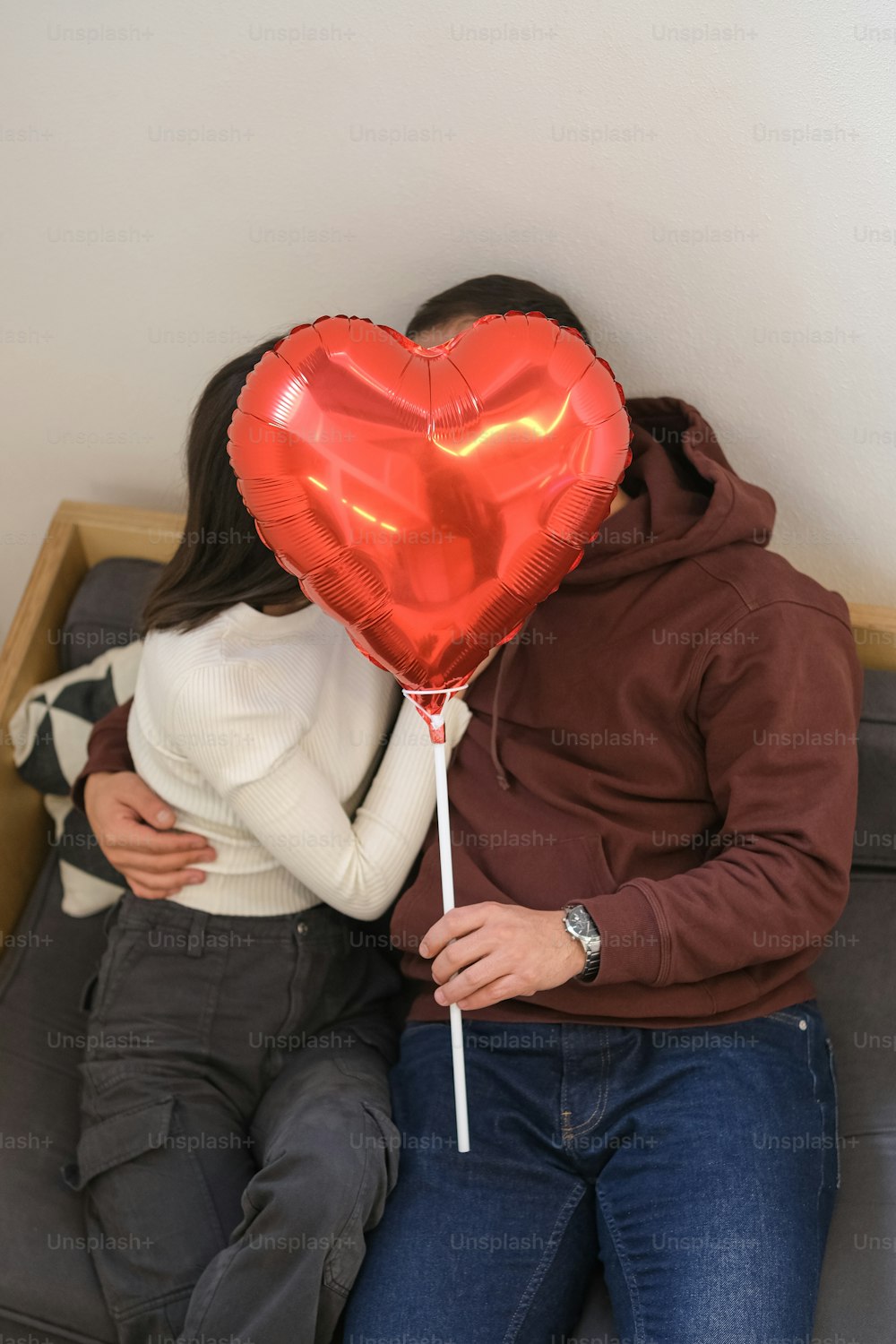 a man and woman sitting on a couch with a heart shaped balloon