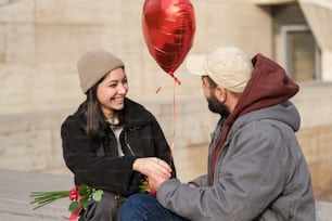 a man holding a red heart shaped balloon next to a woman