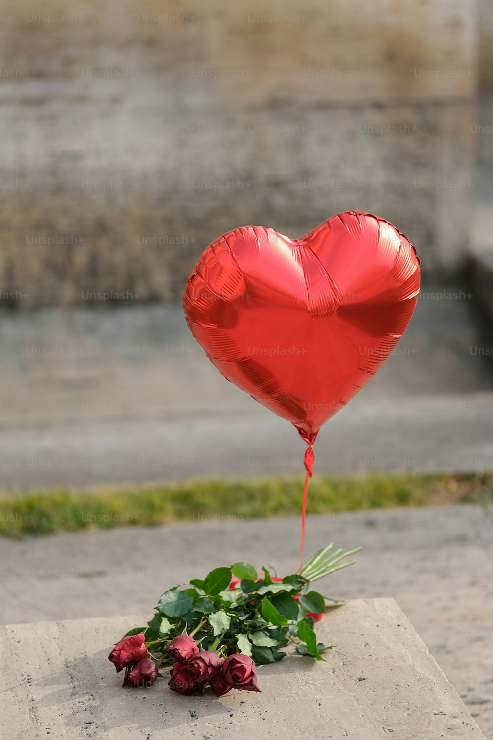 a red heart shaped balloon sitting on top of a cement slab