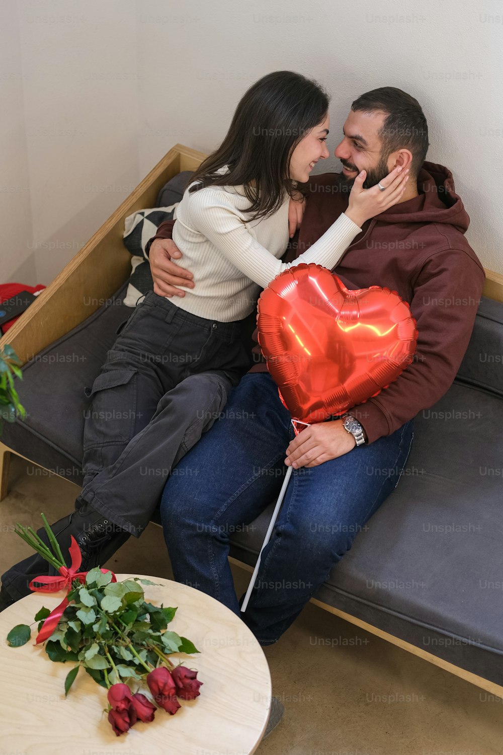 a man and woman sitting on a couch holding a heart shaped balloon