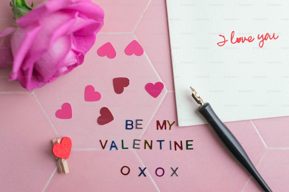 Un biglietto di San Valentino e una penna su sfondo rosa