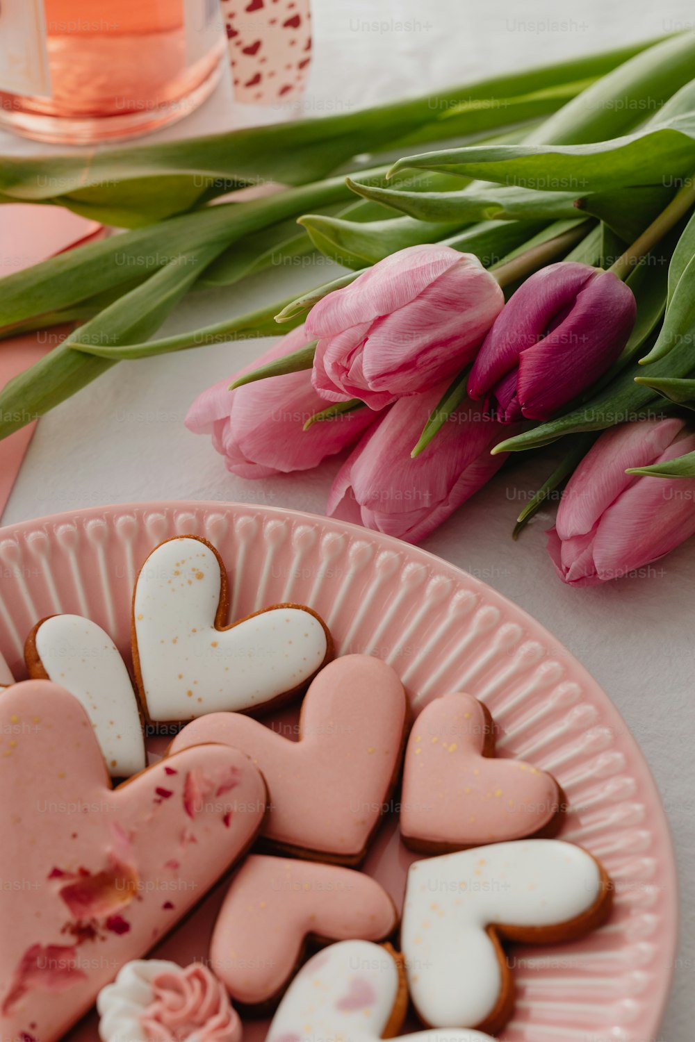 Un plato de galletas en forma de corazón junto a tulipanes rosados