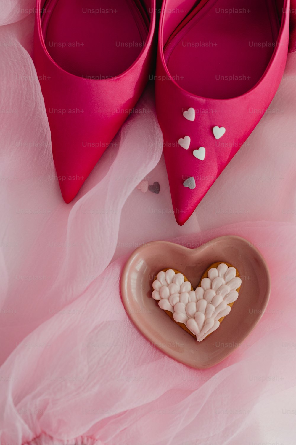 Ein Paar rosa Schuhe neben einem herzförmigen Keks