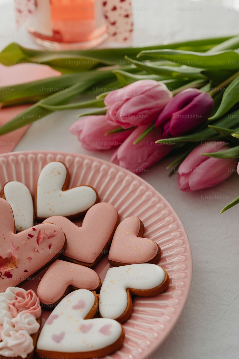 a pink plate filled with heart shaped cookies next to pink tulips