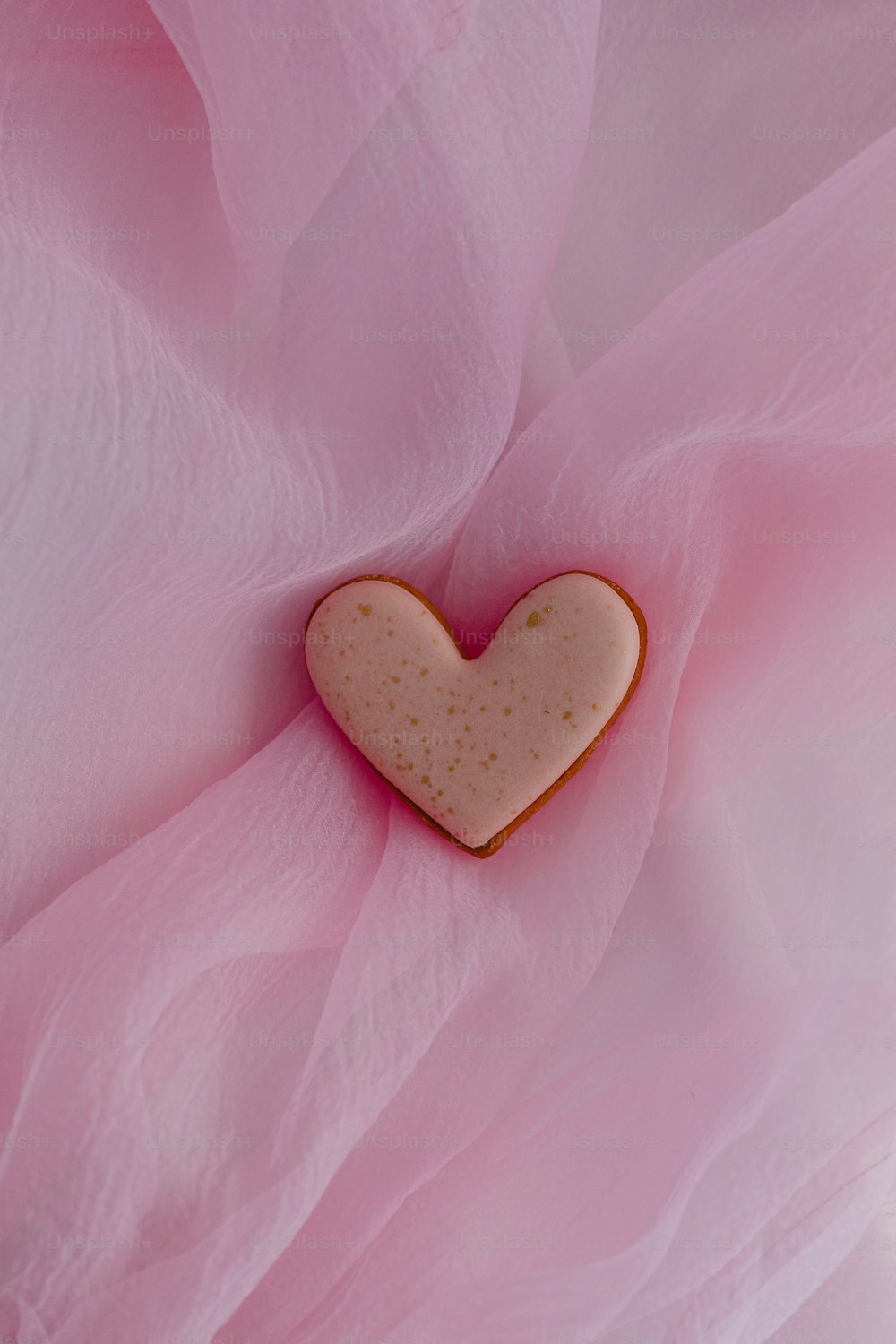 um biscoito em forma de coração sentado em cima de um pano rosa