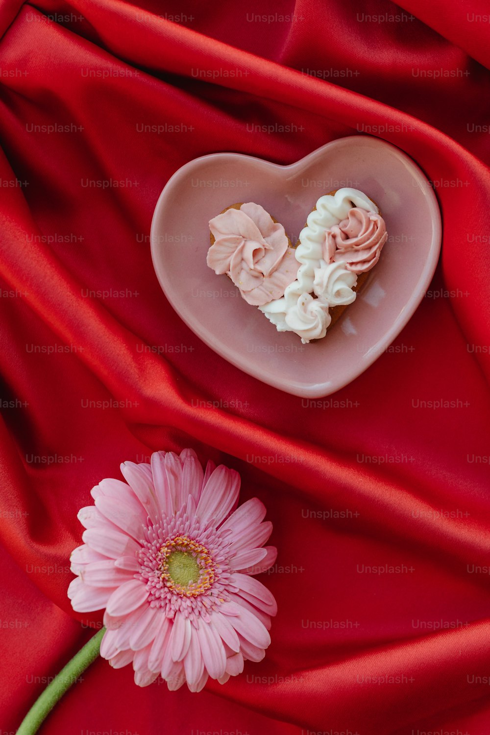 a pink flower and a heart shaped cookie on a red cloth