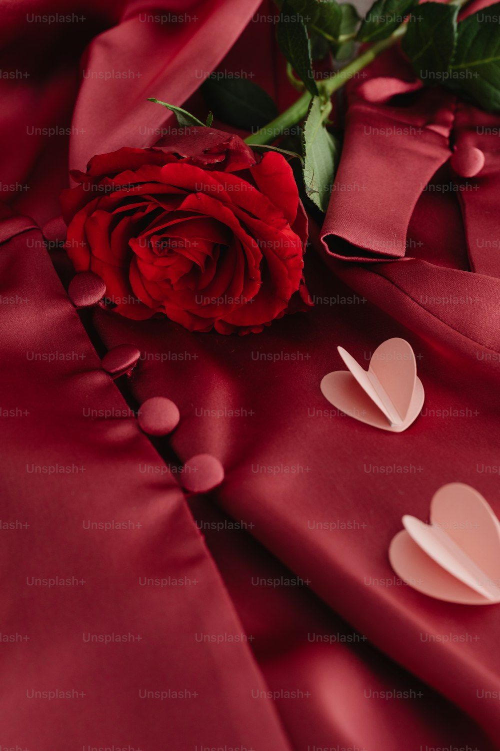 a red rose and two hearts on a red satin