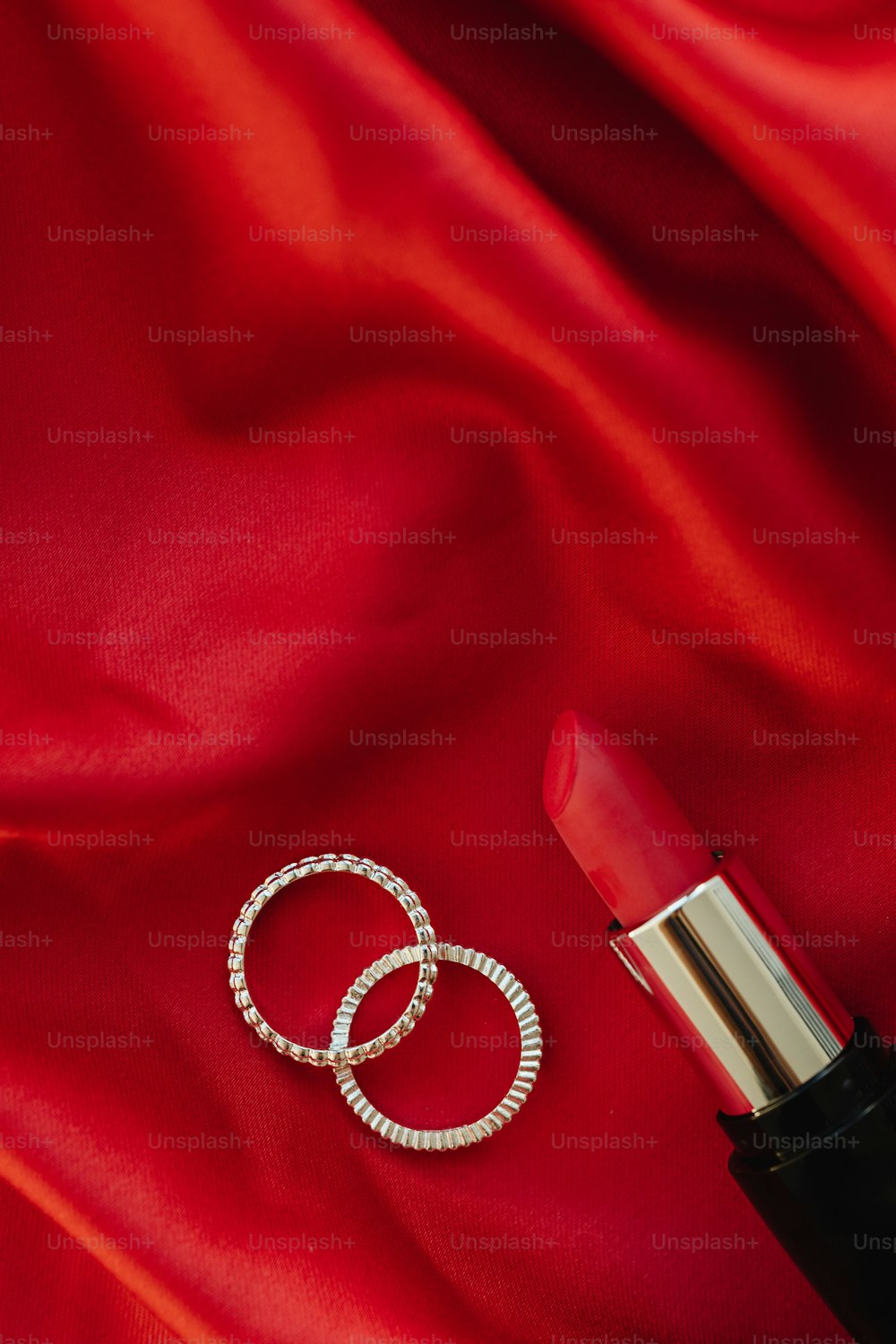a lipstick and two rings on a red cloth