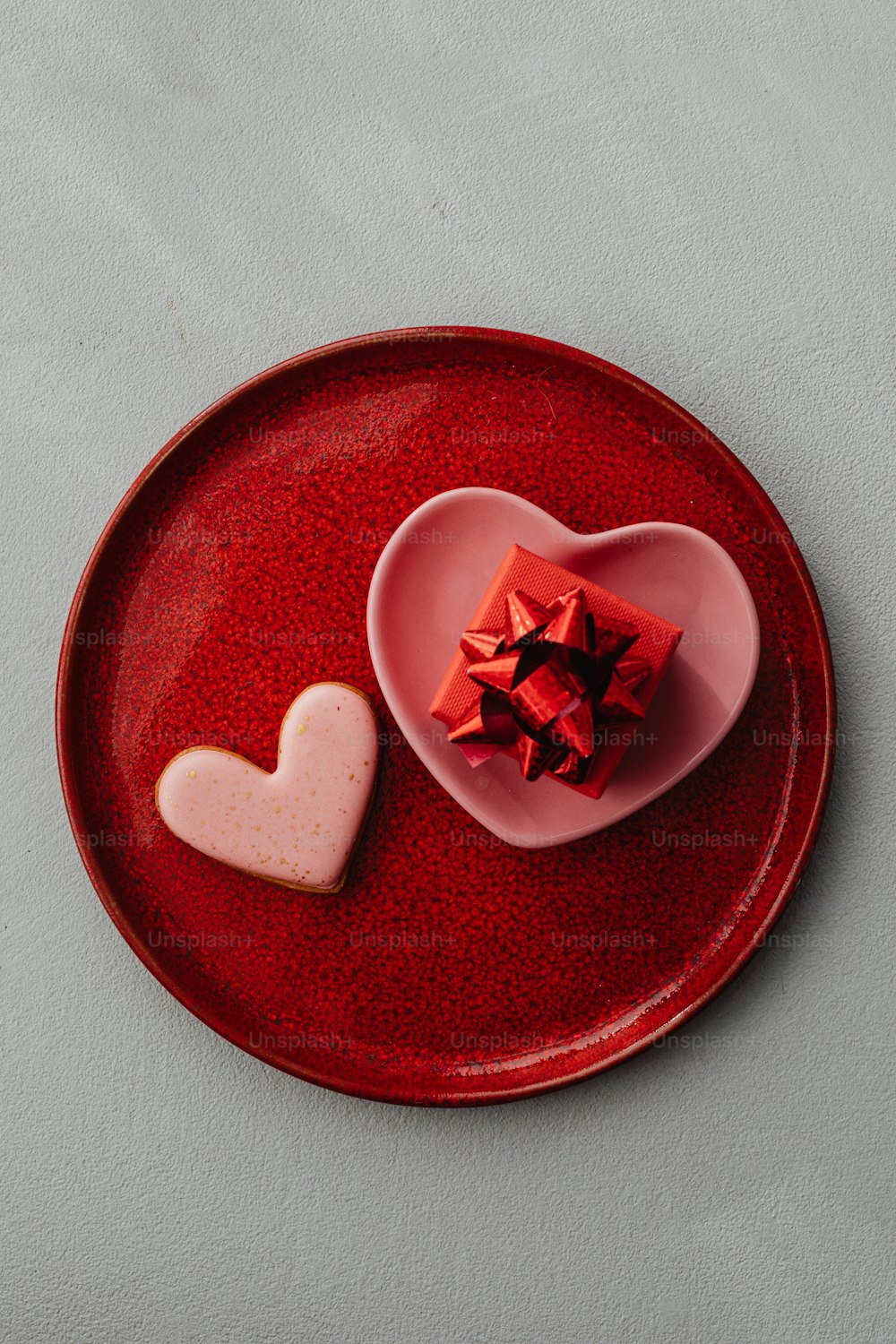 un plato rojo con una caja en forma de corazón y una galleta en forma de corazón