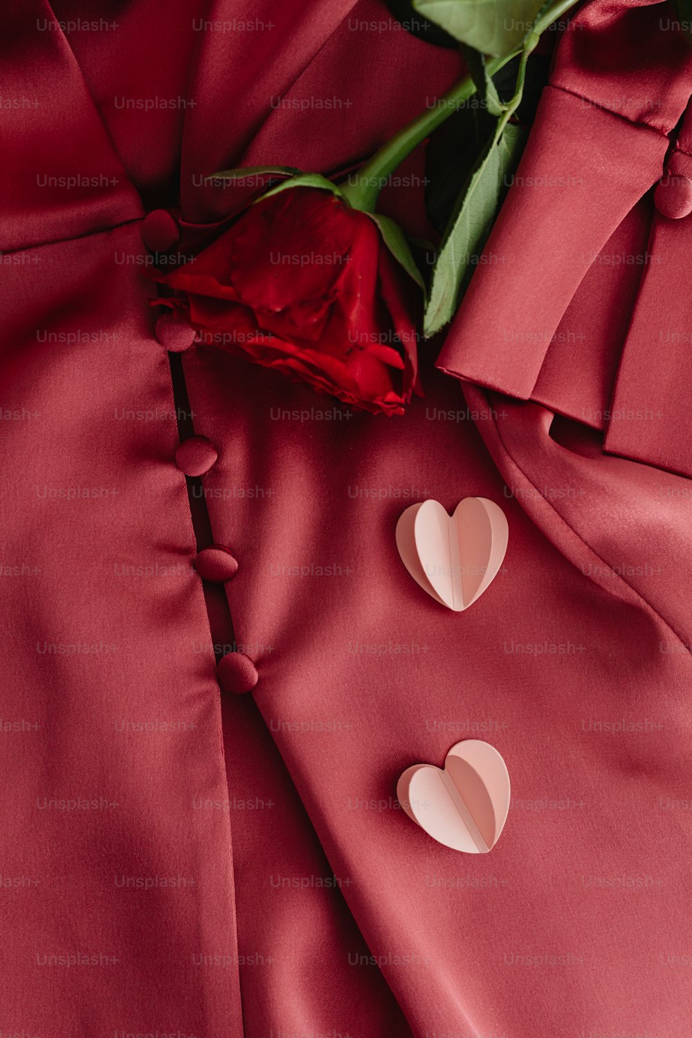 a rose and two hearts on a red satin