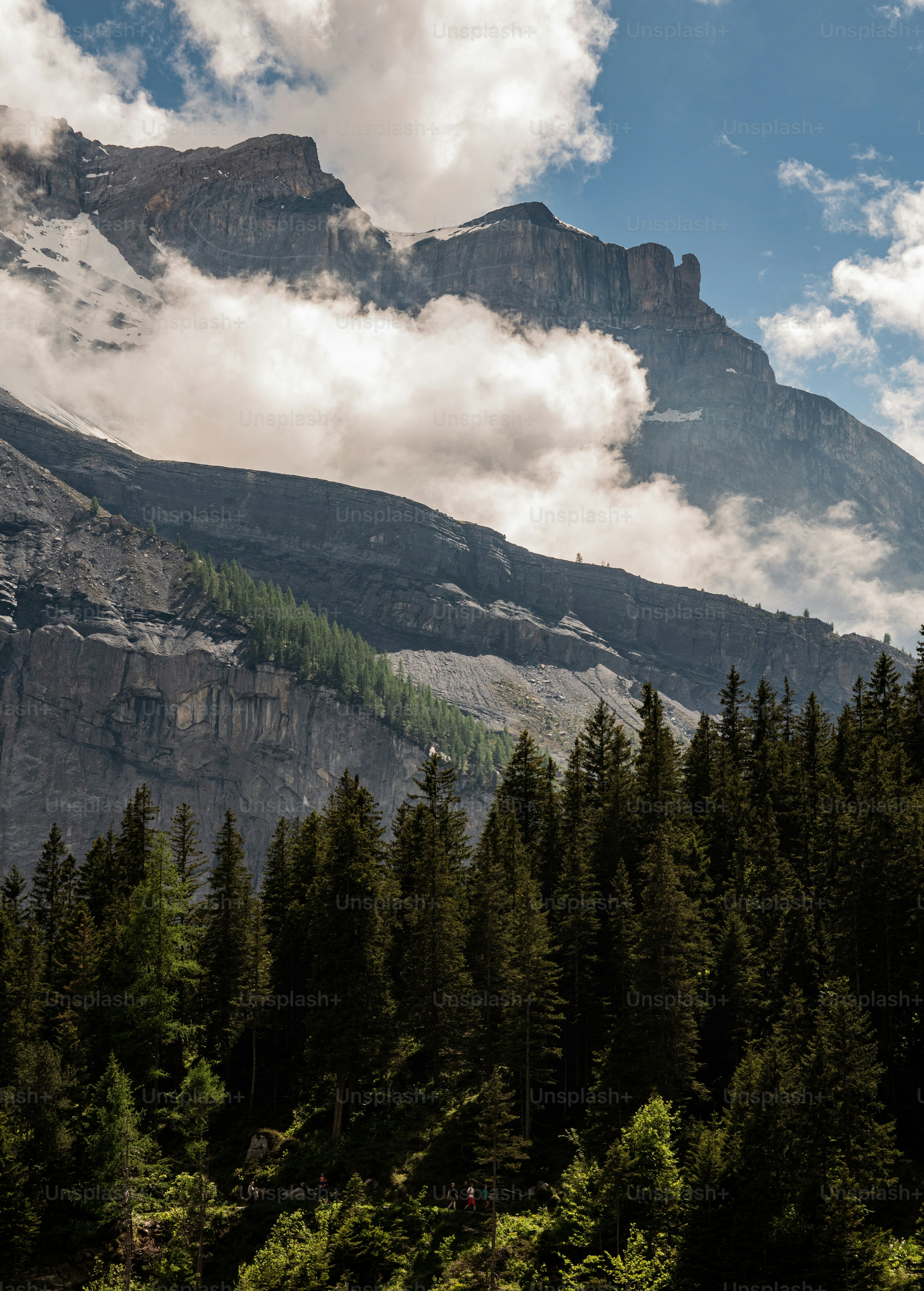 a mountain covered in clouds and trees under a blue sky